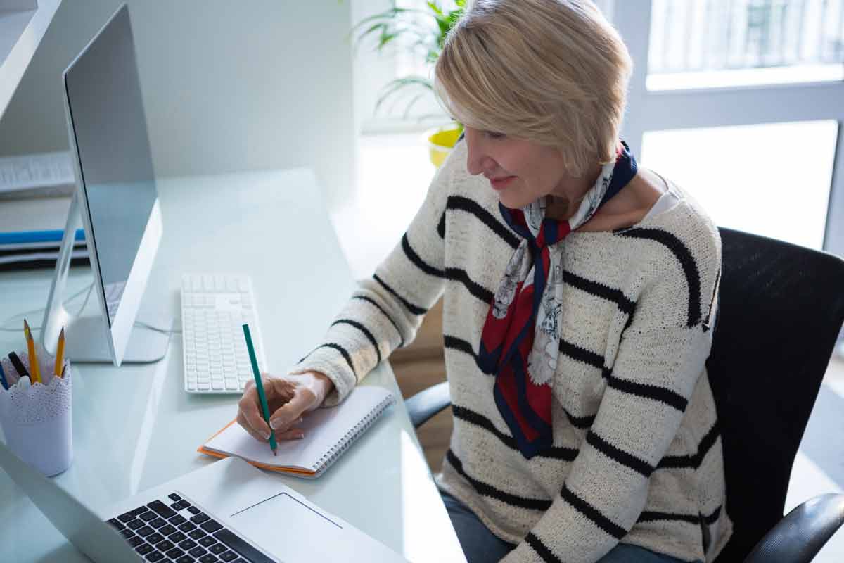 Woman writing in organizer while using laptop